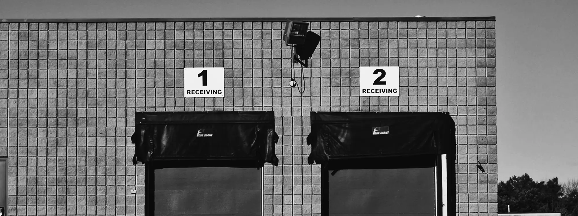 Two numbered receiving doors on a concrete block warehouse wall, shutters raised on the dock seals.